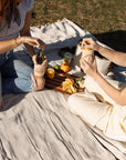 Two people enjoying a picnic on a blanket with food and drinks.