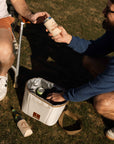 Two people interacting with a cooler bag on grass