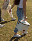 Person carrying a cooler box in a grassy outdoor setting